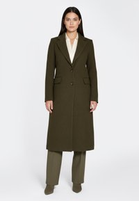 Olivengroene jas van een wolmix met een getailleerd ontwerp, voorzien van een dubbele rij knopen, twee zijzakken en een gladde textuur.