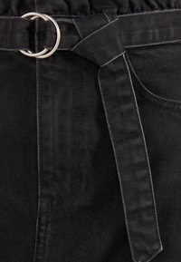 Svart denimtyg med elastisk midja och bälte med en silverfärgad cirkulär spänne, som visar en mjuk textur och rena sömmar.