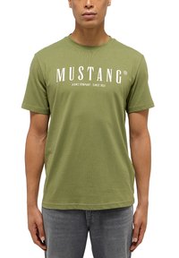 Olívazöld pamut póló, kerek nyakkivágással, rövid ujjakkal, az elején fehér "MUSTANG JEANS COMPANY SINCE 1932" felirattal.