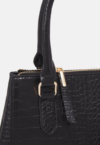Czarna torebka ze skóry ekologicznej z tłoczeniem w krokodila, o zarysowanej konstrukcji, z elementami w kolorze złotym i zamknięciem na zamek błyskawiczny. Posiada krótkie podwójne uchwyty do noszenia.