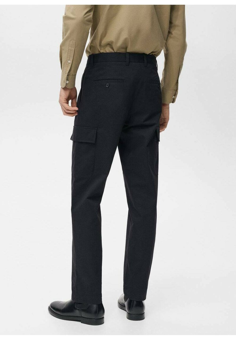 Schwarze Cargo-Hosen mit Seitentaschen, aus robustem Stoff. Schmaler Schnitt mit geradem Bein, kombiniert mit schwarzen Schuhen und einem beigen Hemd.