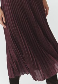 Plissé-Kleid in Burgunderrot mit geometrischem blauen Muster, das eine fließende Silhouette und einen leichten, strukturierten Stoff aufweist.