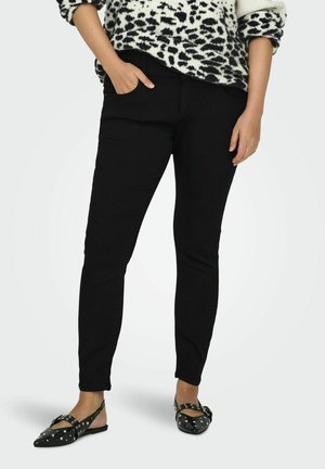 Černé slim-fit džíny s předními kapsami, v kombinaci se strukturou bílo-černého vzorovaného svetru a plochými, studded černými botami.
