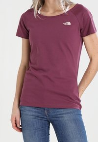 Lyhythihainen maroon-paita pehmeästä puuvillasta, jossa on pyöreä kaula-auko ja The North Face -logo vasemmassa rinnassa. Yhdistetty sinisiin farkkuihin.