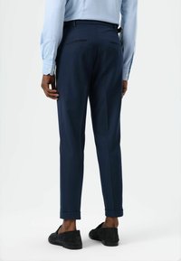 Marineblauwe op maat gemaakte broek met een gladde textuur, een slanke pasvorm en opgerolde manchetten. Voorzien van twee achterzakken met subtiele details. Verstelbare tailleband.