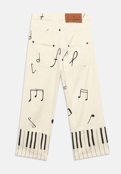 Kremowe spodnie z nadrukiem czarnych nut muzycznych na całej powierzchni i wzorem klawiatury fortepianu na mankietach, ukazane od tyłu.
