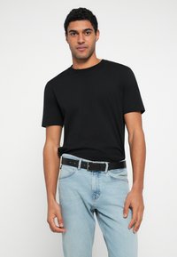 Černé bavlněné tričko s krátkými rukávy, doplněné světle modrými džínami a černým pásem s kovovou přezkou.