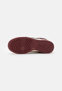 Shoe sole featuring a textured rubber design in maroon with circular patterns and grooves for traction, contrasting a beige outline.