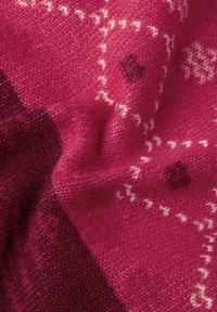 Primer plano de un tejido de punto en tonos rosa y burdeos con patrones geométricos y circulares, mostrando detalles de textura y trenzado.