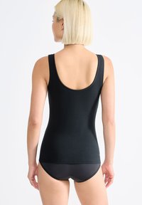 Černý přiléhavý top bez rukávů s širokými ramínky, hladkou texturou a zakulaceným výstřihem, v kombinaci s černými kalhotkami. Pohled zezadu.