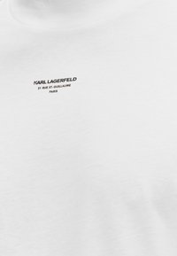 Λευκό ύφασμα με μικρό μαύρο κείμενο "KARL LAGERFELD 21 RUE ST-GUILLAUME PARIS" στο κέντρο κοντά στην κορυφή.