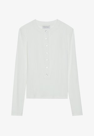 Haut à manches longues blanc en tissu côtelé, avec un col rond et un devant boutonné comportant six boutons transparents.