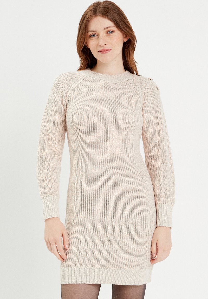 Vestido de punto en beige claro, con textura acanalada, mangas largas y detalles de botones en el hombro, con una silueta ajustada.