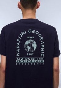 Mørkeblå bomulds t-shirt med et rundt grafik af en globe og teksten "Napapijri Geographic Since 1987" i lys grøn.