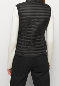 Svart puffer-väst med horisontell söm, hög krage och lätt material. Har en liten logotyp nära fållen och sidofickor.