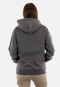 Felpa grigia scura con un ampio cappuccio, vestibilità ampia e polsini e orlo a costine. Il tessuto appare morbido e leggermente texturizzato. Nessun marchio visibile.