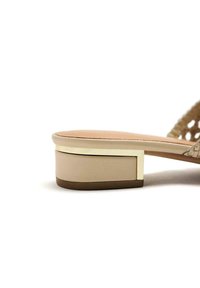 Sandalia de plataforma beige con un tacón grueso, presentando una textura suave y un detalle dorado alrededor del tacón. Diseño abierto con detalles trenzados.