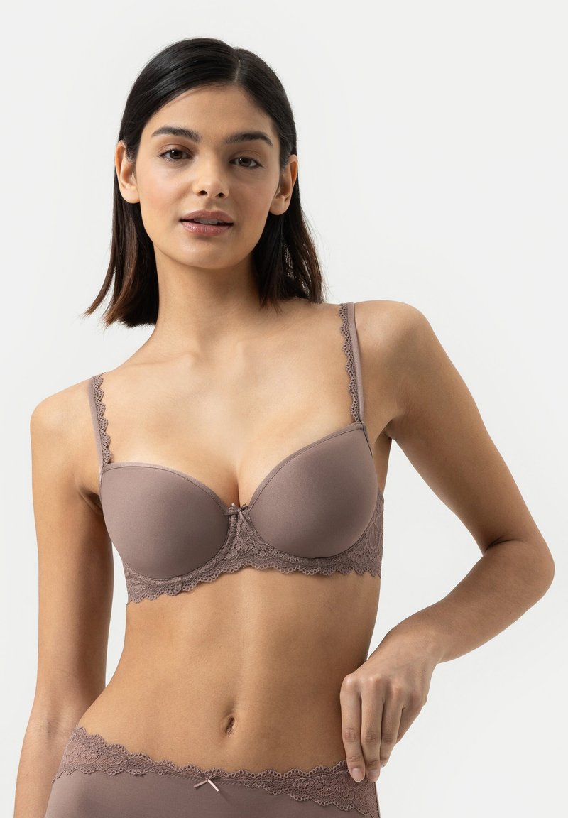 Pusero- ja rintaliivit pehmeässä mauve-värisessä kankaassa, jossa on pitsireunus, kaarituki ja säädettävät hihnat. Sisältää pienen keskellä olevan nauhaketjun yksityiskohdan.