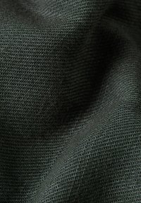 Tessuto verde scuro e strutturato che mostra un motivo tessuto. Il materiale sembra morbido con una leggera lucentezza, evidenziando i dettagli intricati del tessuto.