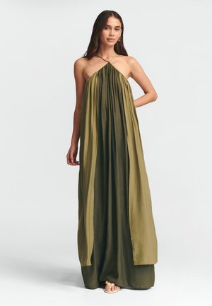 Abito maxibra verde oliva, senza maniche, con tessuto arricciato, design a collare all'americana, silhouette fluida e texture morbida. Indossato con sandali semplici.