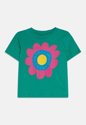 Grøn kortærmet t-shirt med stort pink blomstermotiv, blå cirkulær midte og gul rund kerne med tekst omkring.