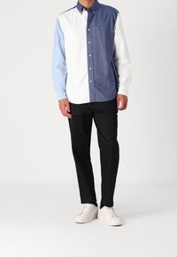 Camicia con bottoni caratterizzata da un design a blocchi di colore: bianco, azzurro chiaro e blu scuro. Tessuto in cotone, maniche lunghe e taschino a sinistra sul petto.