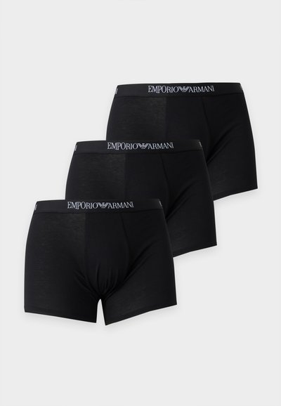 Trois boxers noirs pour hommes avec le logo Emporio Armani sur la ceinture, disposés en chevauchement sur un fond clair.