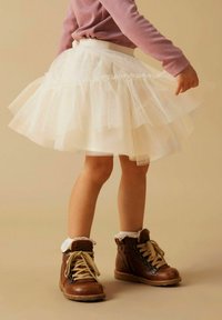 Bjela tulle suknja s višeslojnim volanima, elastičnim pojasom i smešnim čizmama do gležnja s čipkastim dizajnom i bijelom krznenom podstavom.