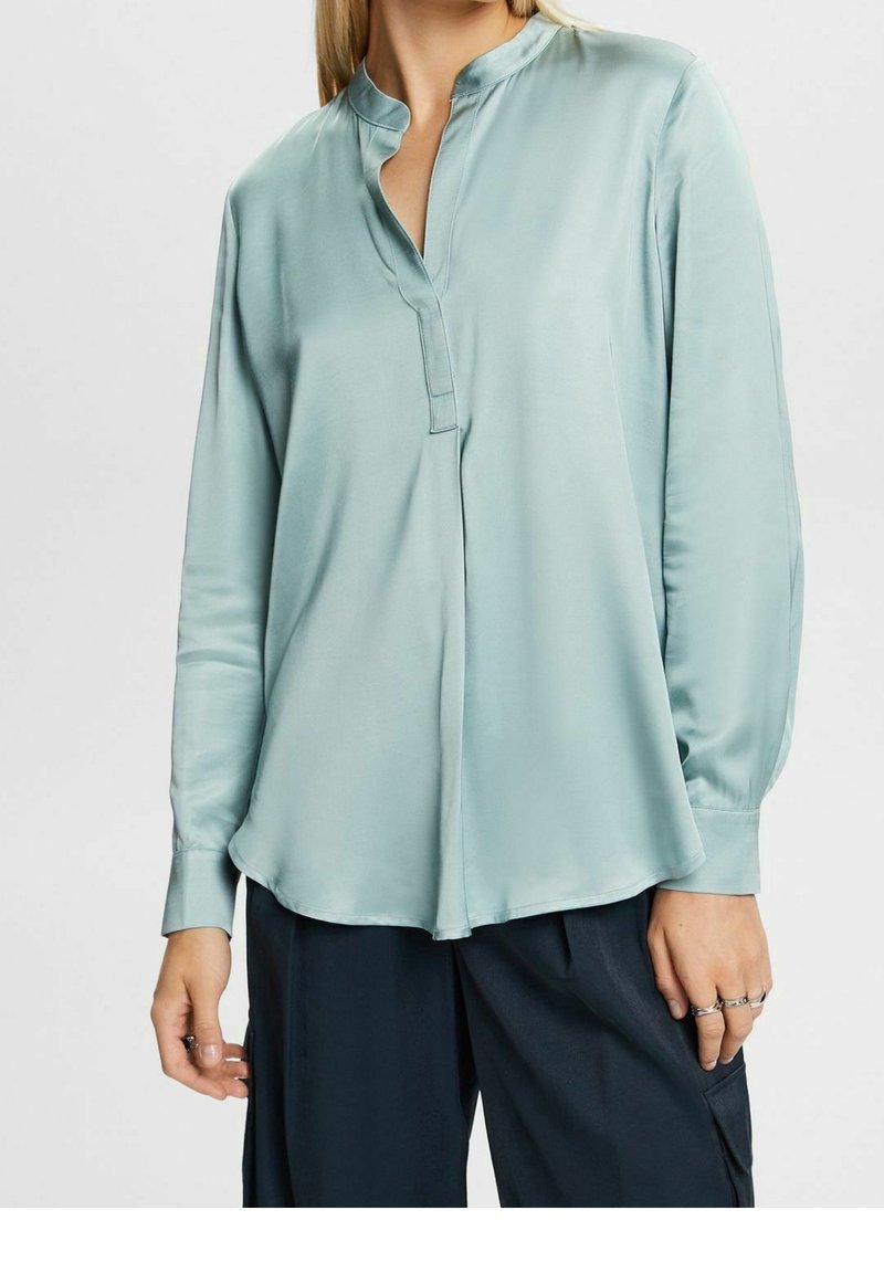 Turkos satinblus med ståkrage och knapplist. Långa ärmar med manschetter, rundad nederkant och slät textur.