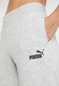Szare dresowe spodnie uszyte z miękkiego materiału mają elastyczny pas, boczne kieszenie oraz czarny nadrukowany logo na lewej udzie.