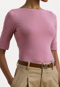 Top rosa justo com mangas até ao cotovelo e um decote largo, combinado com calças beiges de cintura alta e um cinto castanho com uma fivela prateada.