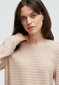 Hellbeiges Langarmshirt aus strukturiertem Stoff mit horizontalem Rippenmuster und rundem Ausschnitt, an den Ärmelbündchen leicht tailliert.