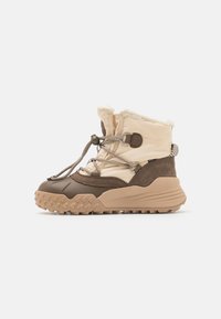 Brune en crèmekleurige enkelboots met een getextureerde rubberen zool, zachte nepbontvoering, decoratieve veters en suède accenten.