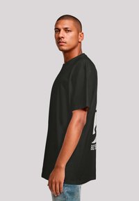 Schwarzes Baumwoll-T-Shirt mit kurzen Ärmeln, das auf der Rückseite mit einem großen weißen Grafikdruck versehen ist. Lockerer Schnitt und Rundhalsausschnitt.