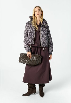 Frau trägt eine Leopardenprint-Reißverschlussjacke, ein dunkelbraunes langes Kleid, lässige braune Stiefel und hält eine große dunkelbraune Lederclutch.