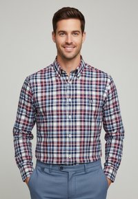 Camisa de cuadro en tonos rojo, marino y blanco, con un collar clásico y un bolsillo en el pecho, combinada con pantalones texturizados en azul claro.