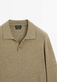 Beige Woll-Polohemd mit kragenförmigem Ausschnitt, einer Zwei-Knopf-Leiste und strukturiertem Stoff. Verfügt über ein Etikett an der Innenseite des Kragens.