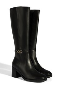 Bottes noires en cuir montant jusqu'au genou avec un talon bloc, ornées d'une chaîne dorée au niveau de la cheville et d'une texture lisse.