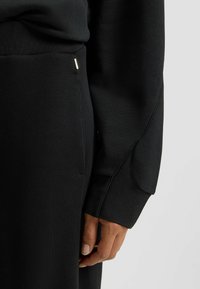 Svart sweatshirt med avslappnad passform, ribbade ärmar, mjuk textur och en subtil metallisk detalj på sid sömmen.