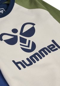 Kortärmad skjorta med krämfärgad kropp, gröna ärmar och marinblå logotyp med styliserad bidesign och varumärket "hummel" i fet stil.