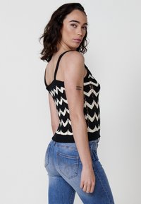 Top in maglia a righe chevron bianco e nero con spalline sottili e una silhouette aderente, abbinato a jeans di denim azzurro chiaro.