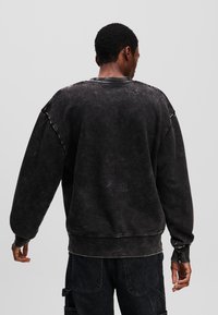Sort oversized sweatshirt, falmet tekstur, ribbede manchetter og bund, synlig syning, afslappet pasform, båret med mørke cargo-bukser.