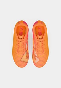 Vividni oranži futbola apavi ar teksturētu virsu, uzsvērti ar rozā akcentiem un melnu logo. Ar auklām, ar elegantu, plūstošu formu.