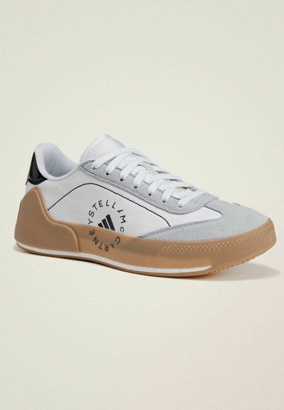 White and gray sneakers with a textured upper, black heel accent, and gum rubber sole featuring a distinctive logo and stitching details.