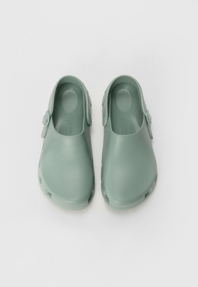 Zoccoli verde menta realizzati in materiale sintetico liscio, dotati di una fascia posteriore e fori di ventilazione sui lati per una migliore traspirabilità.