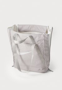 Sac fourre-tout en tissu gris avec deux poignées grises, arborant un logo Nike blanc bien visible. Il a une forme rectangulaire structurée et se ferme par zip.