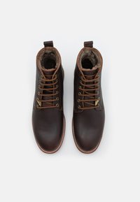 Botas de tobillo de cuero marrón con cordones marrones, acentos en tono claro y forro suave. Cuentan con una punta redondeada y una lengüeta en la parte superior para facilitar su uso.