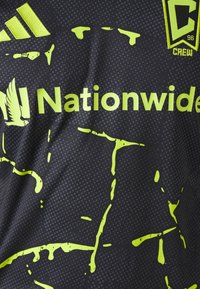 Camisa deportiva negra con gráficos en amarillo neón, que incluyen un logo de la marca y el texto "Nationwide". Tejido suave con una textura punteada.