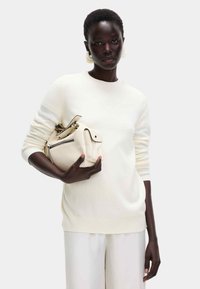 Kremowy sweter z dzianiny z prążkowanymi mankietami, zestawiony z usztywnioną torbą w jasnym beżu z zamkniętą kieszenią i uchwytami.