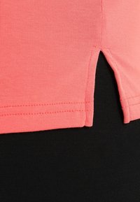 Närbild av korallrosa tygslut med sidöppning över svart ribbat tyg.